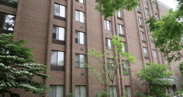 Park Heights exterior — six-story brick apartment building with bay windows framed by mature trees and flowering dogwoods