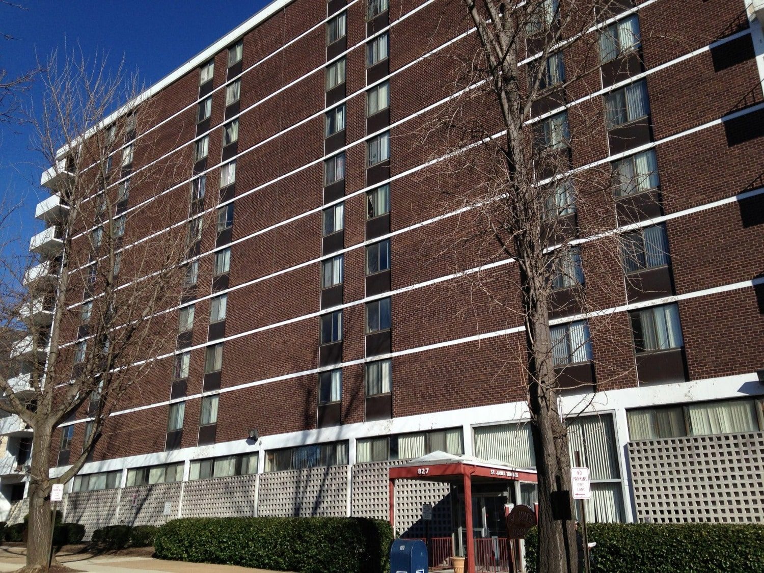 St. James Apartments exterior — seven-story red-brick high-rise affordable housing building with white banding and a red entry canopy at 827