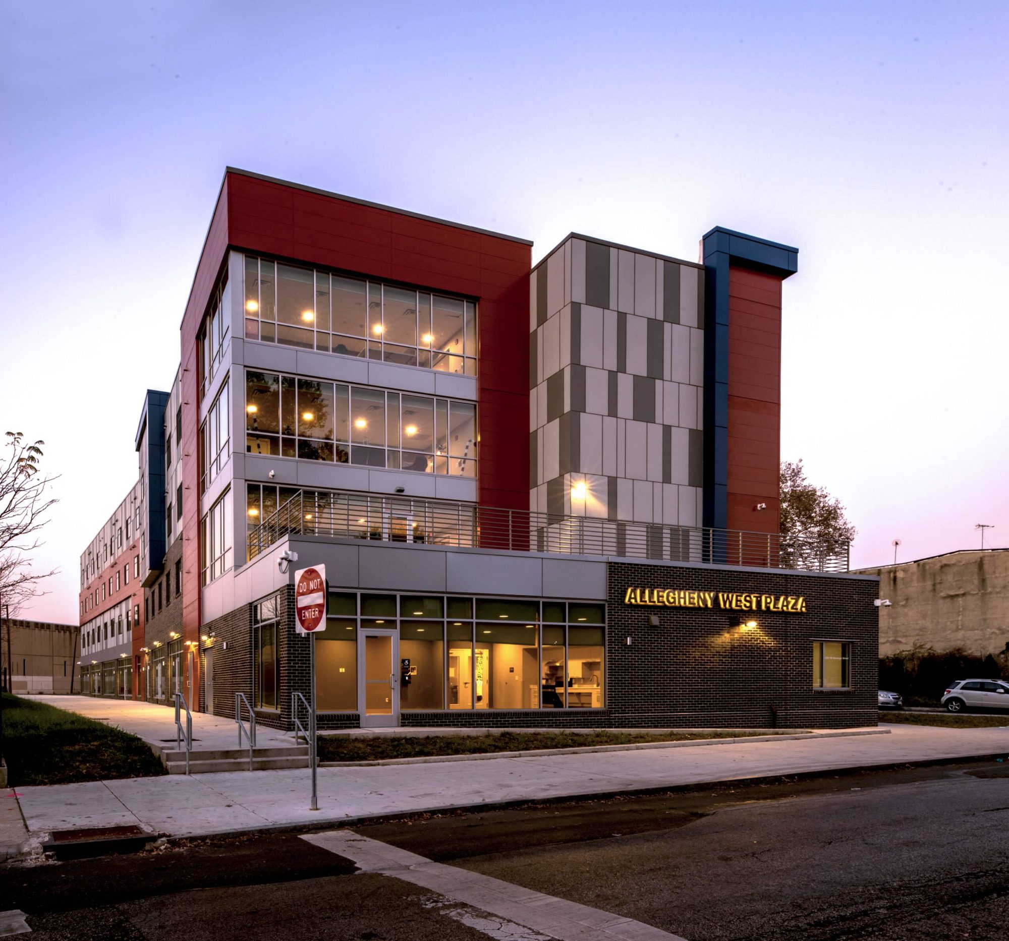 Allegheny West Plaza exterior at dusk with illuminated signage and red metal-panel façade