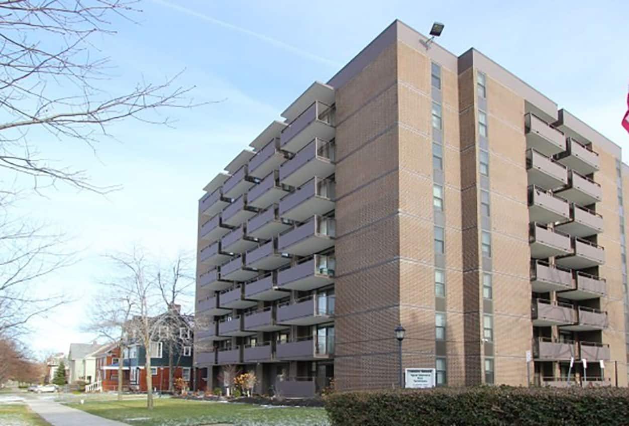 Trinity Towers exterior — eight-story brick affordable housing high-rise with stacked private balconies and adjacent residential homes