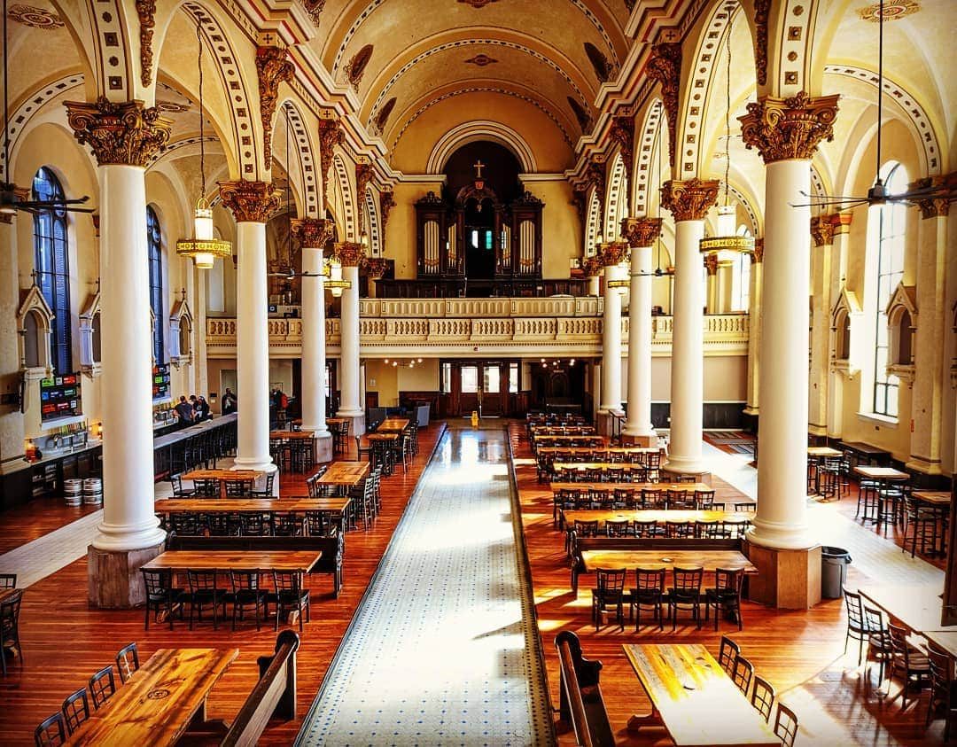 Ministry of Brewing taproom inside a restored historic church with Corinthian columns, vaulted ceiling, and communal seating