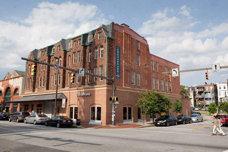 The Chesapeake — restored historic red-brick mixed-use building on a Baltimore corner with ground-floor retail signage