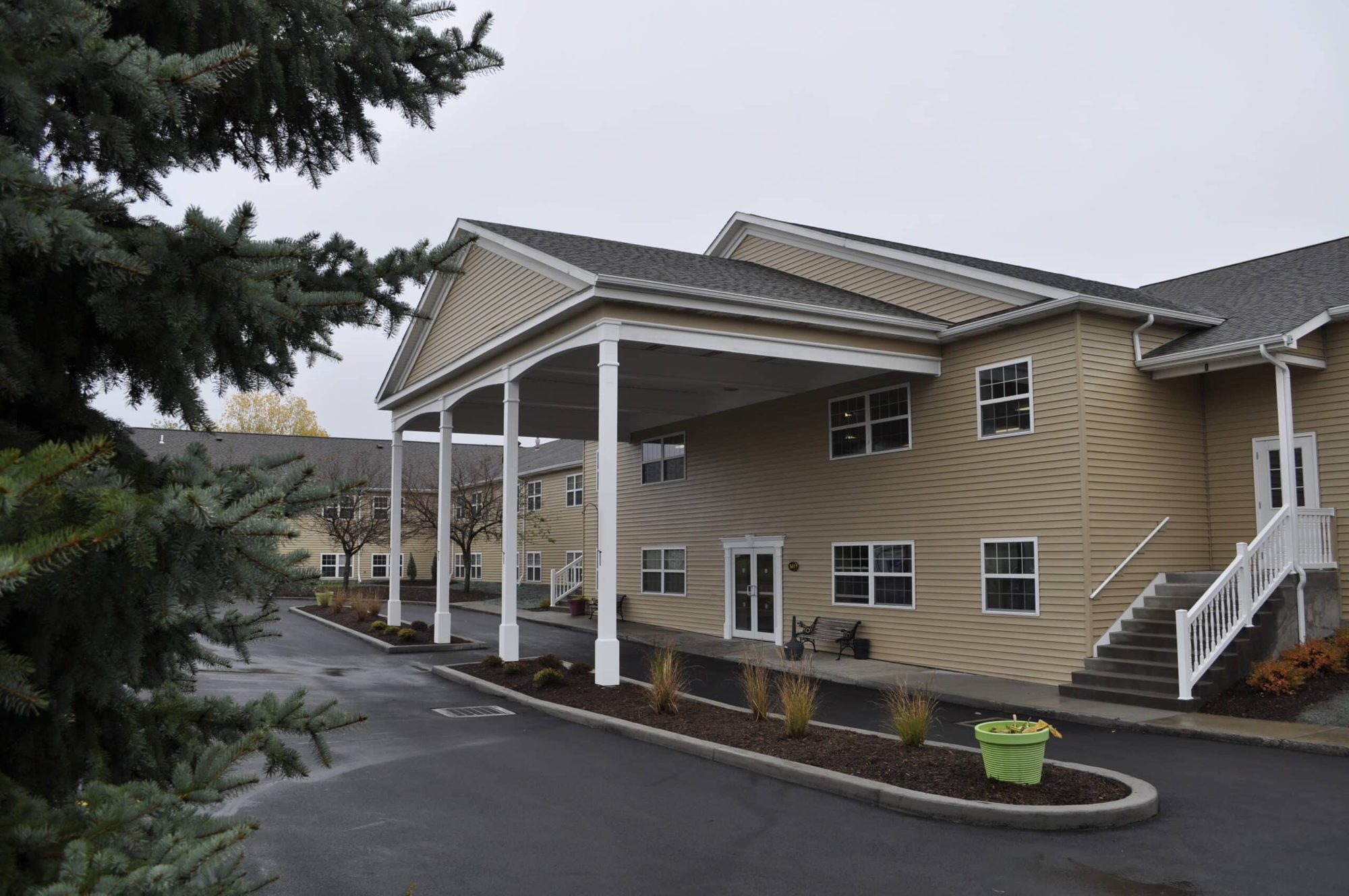 Walden Park entrance — two-story tan-sided senior housing building with a covered porte-cochère, white columns, and landscaped drive in Buffalo